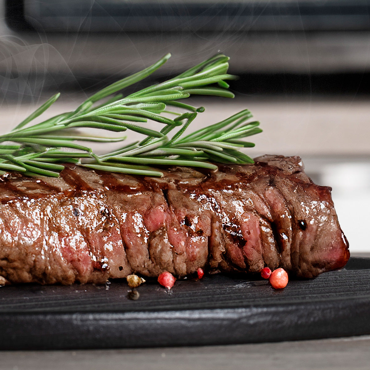 Gegrilltes Steak mit frischen Rosmarinzweigen auf schwarzem Teller  