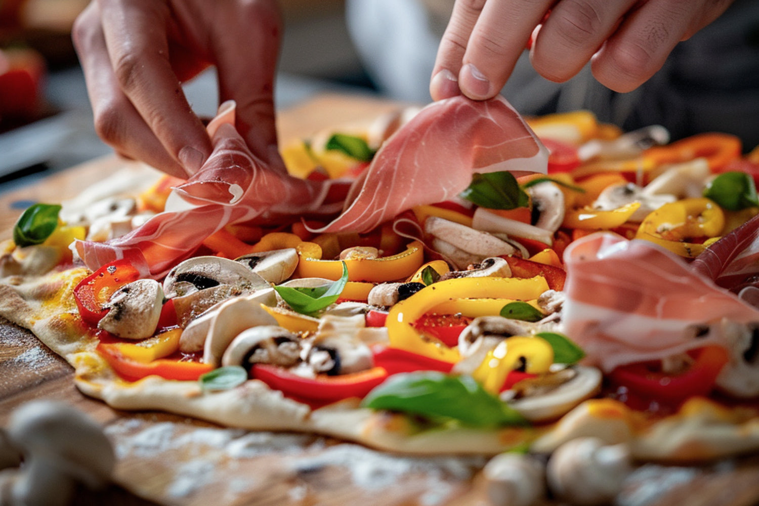 Hände dekorieren Pizza mit Paprika, Champignons, Basilikum und Prosciutto auf Holzarbeitsplatte